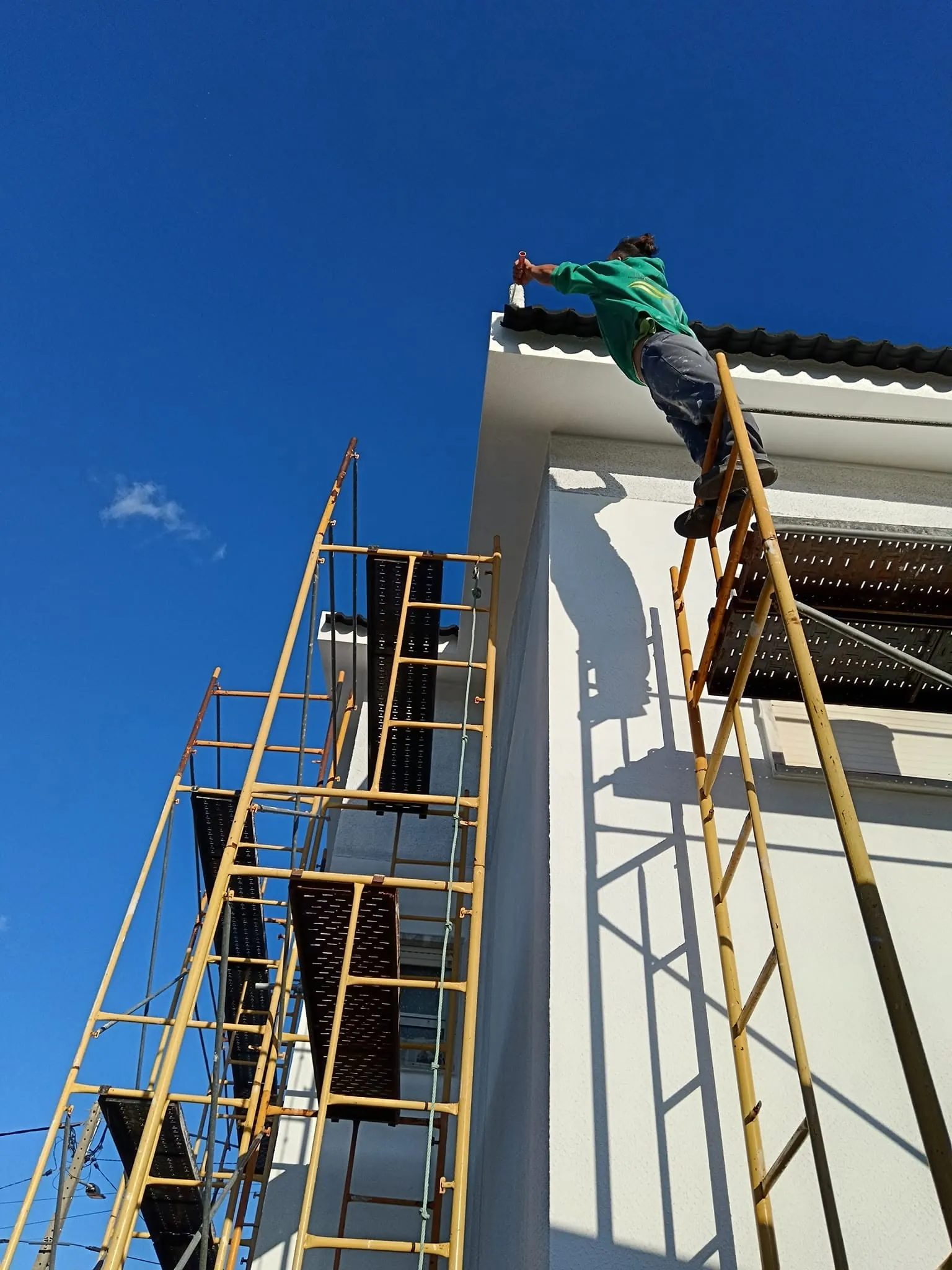 Pintor em andaime a dar acabamento ao beirado de uma moradia